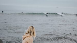 Woman sitting, staring contemplatively at waves of the ocean