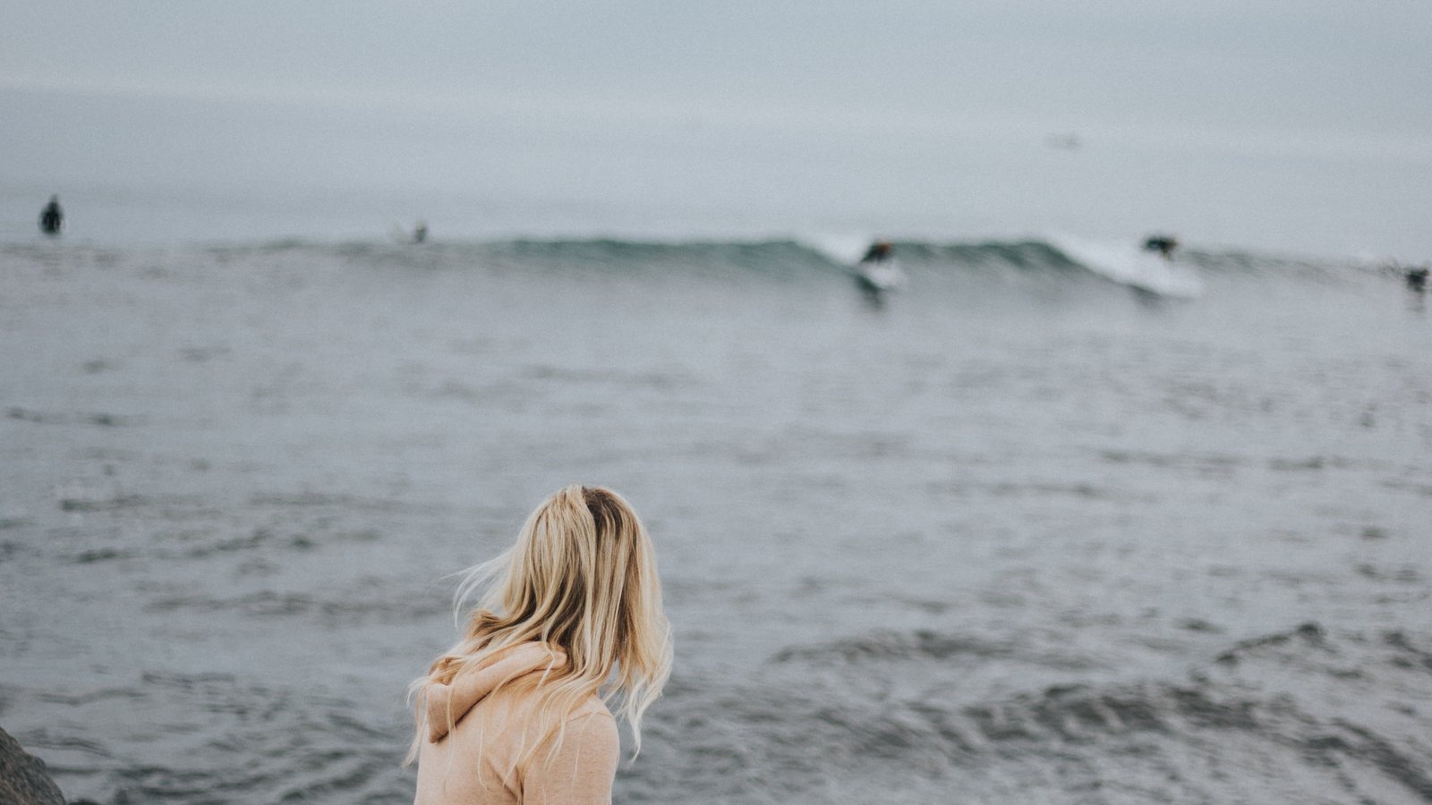 Woman sitting, staring contemplatively at waves of the ocean